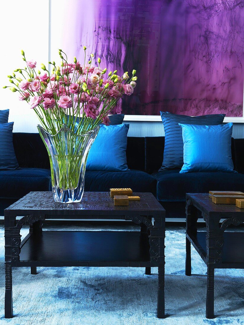 Rosa Blumenstrauss in einer Glasvase vor dunkelblauer Samtcouch mit blauen Seidenkissen und darüberhängendem violetten Wandbehang