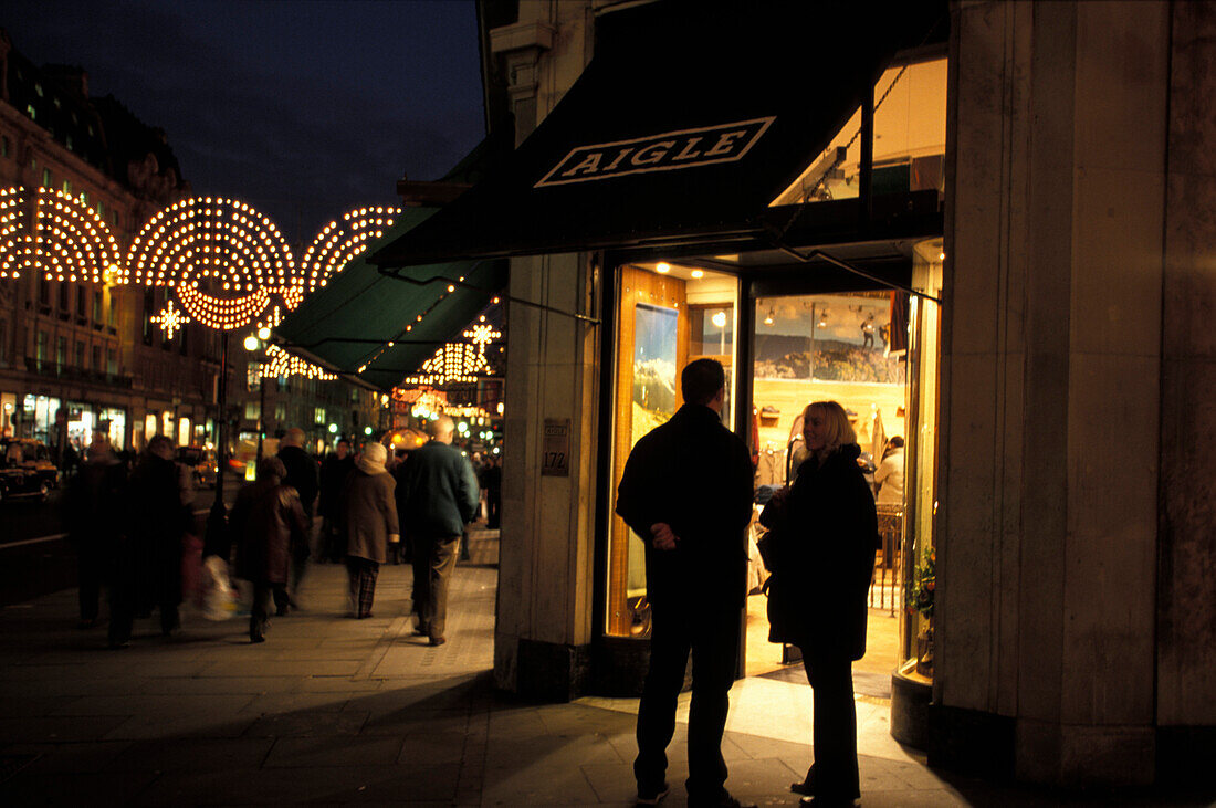Menschen vor einem beleuchteten Geschäft am Abend, Regent Street, London, England, Grossbritannien, Europa