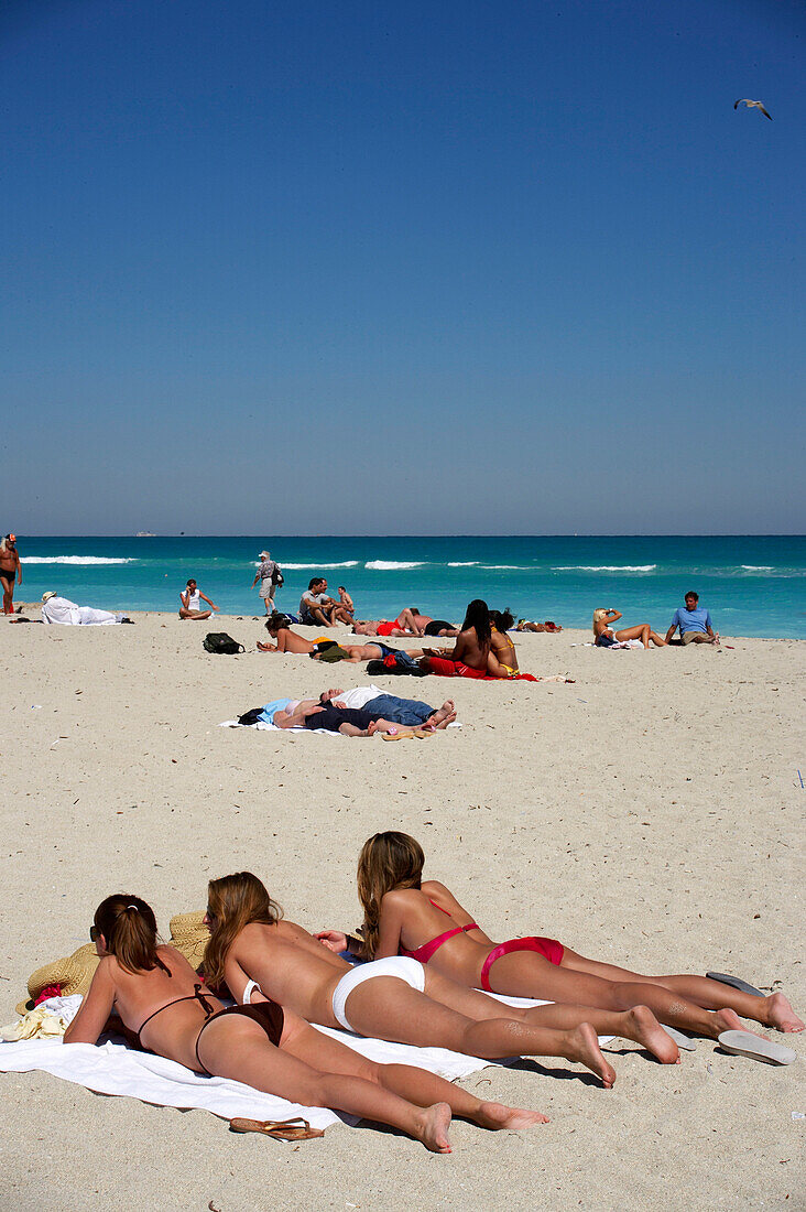 Drei junge Frauen liegen in der Sonne, Strandleben, Art Deco Altstadt, South Beach, Miami, Florida, USA