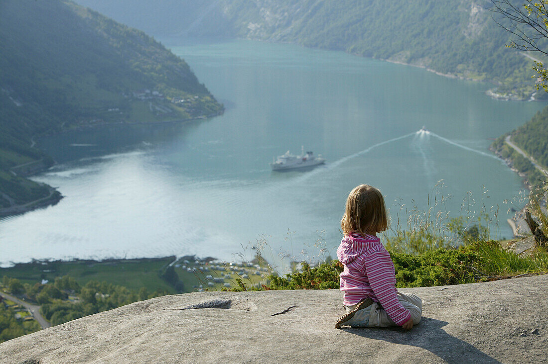 Mädchen sitzt an den Felsen über Geiranger Fiord, More og Romsdal, Norwegen