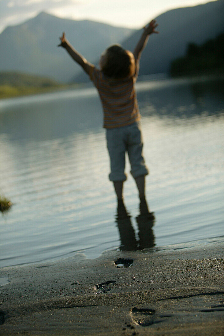 Child with outstretched arms on the beach at lake vaga, near Lom, Oppland, Norway