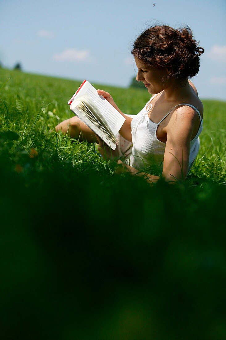 Young Woman reading book on lawn, bavaria Germany