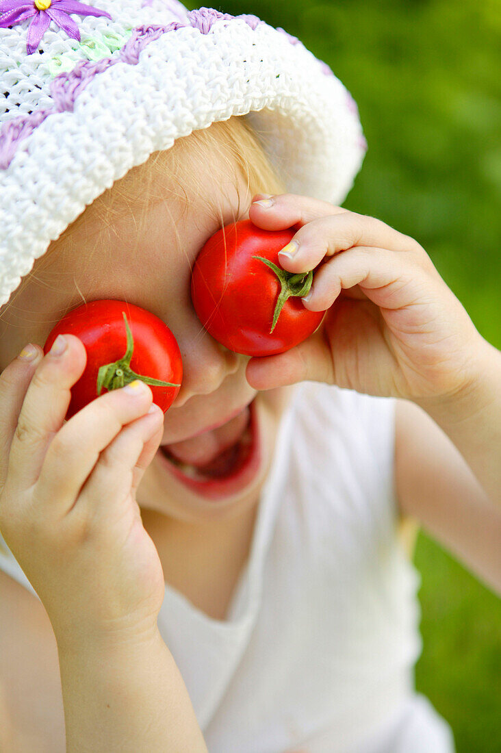 Kleines Mädchen mit Tomaten auf den Augen