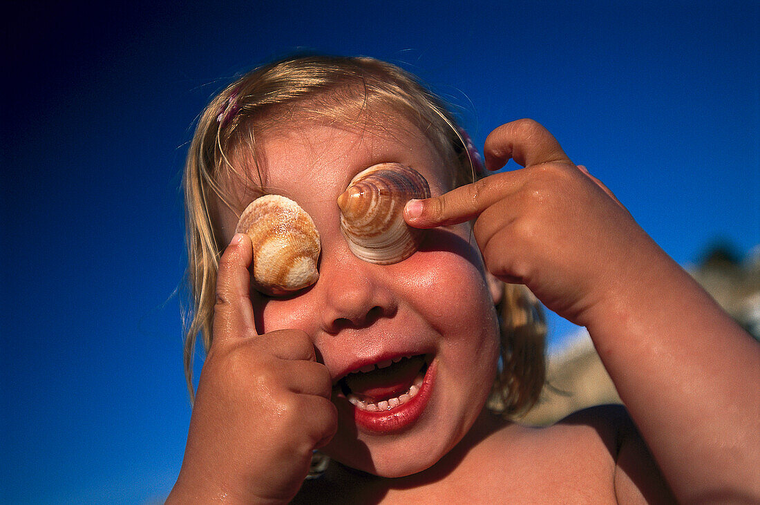 Mädchen bedeckt ihre Auge mit Muscheln, Cala S. Vicente, Mallorca, Balearen, Spanien