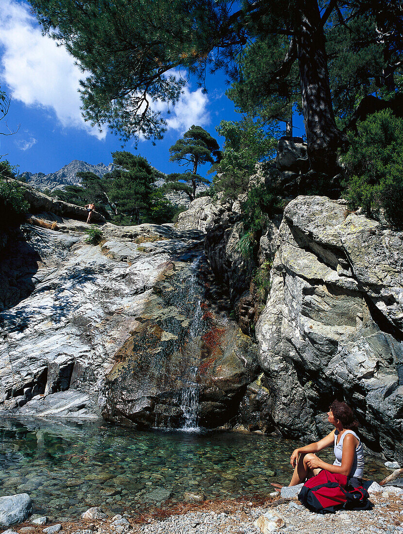 Woman sitting feet in water near waterfall, Cascades des Anglais, Corsica, France