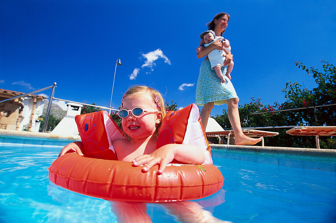 Girl with sunglasses, waterwings and Floating Tire swimming in pool, Mallorca