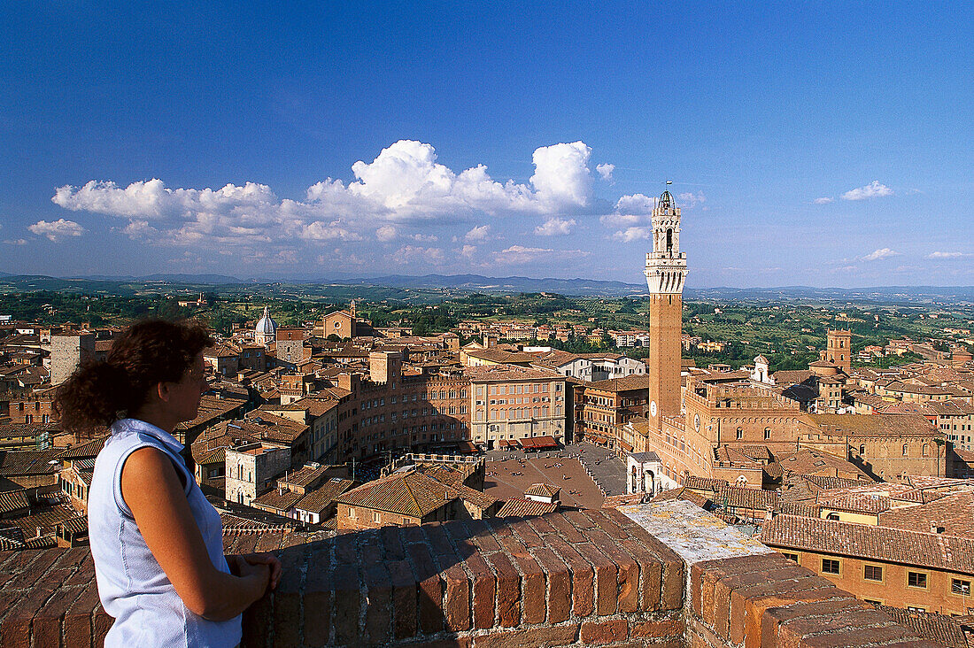 Woman overlooking city rooftops with Piazza del Campo and Torre del Mangia, Siena, Tuscany, Italy