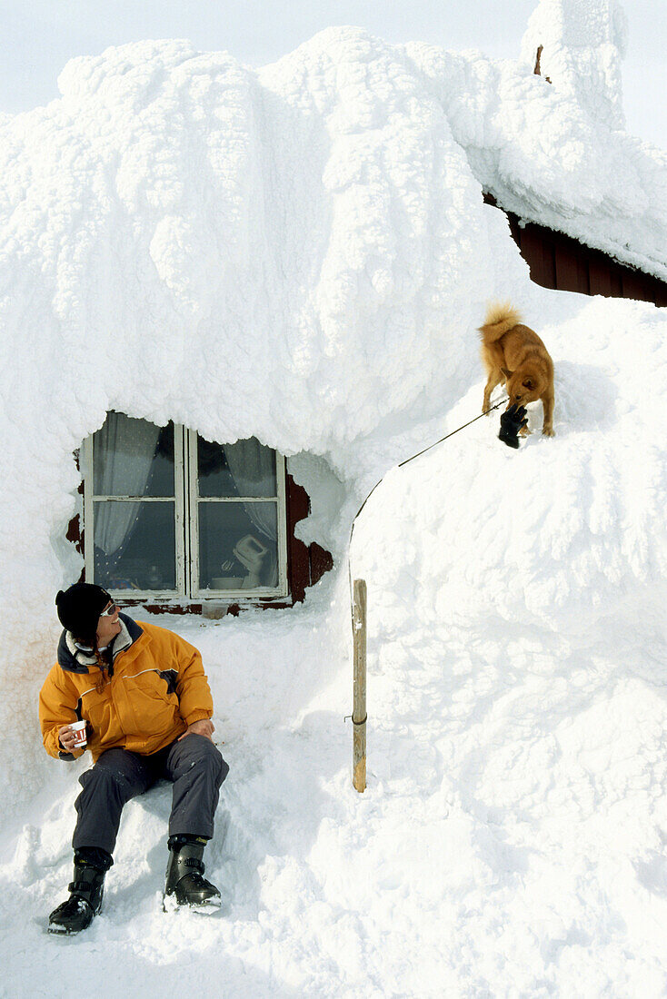 Mann mit Hund vor eingeschneiter Berghütte, Areskutan, Are, Sweden