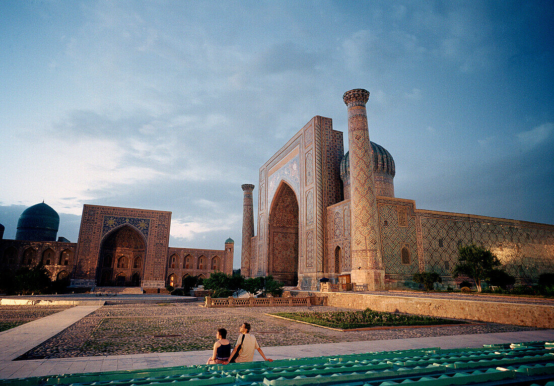 Tourist couple sitting on Registan Square at dusk, Samarkand, Uzbekistan