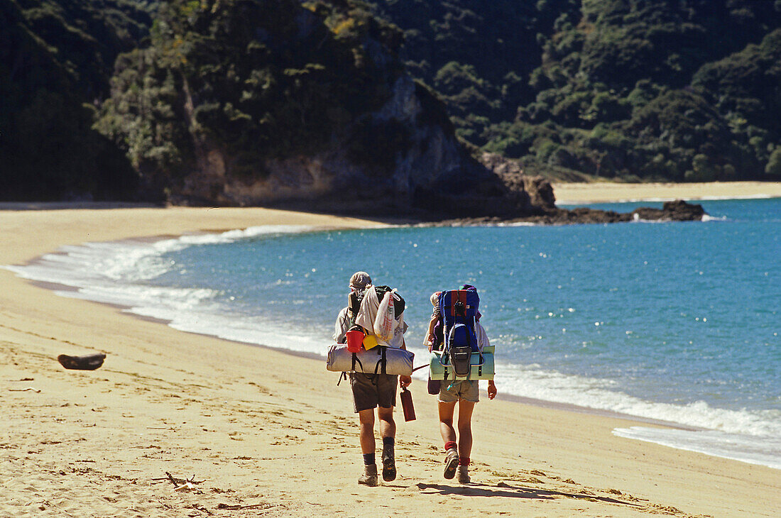 Wanderer mit Rucksack am Strand im Sonnenlicht, Abel Tasman Coast Track, Abel Tasman Nationalpark, Neuseeland, Ozeanien