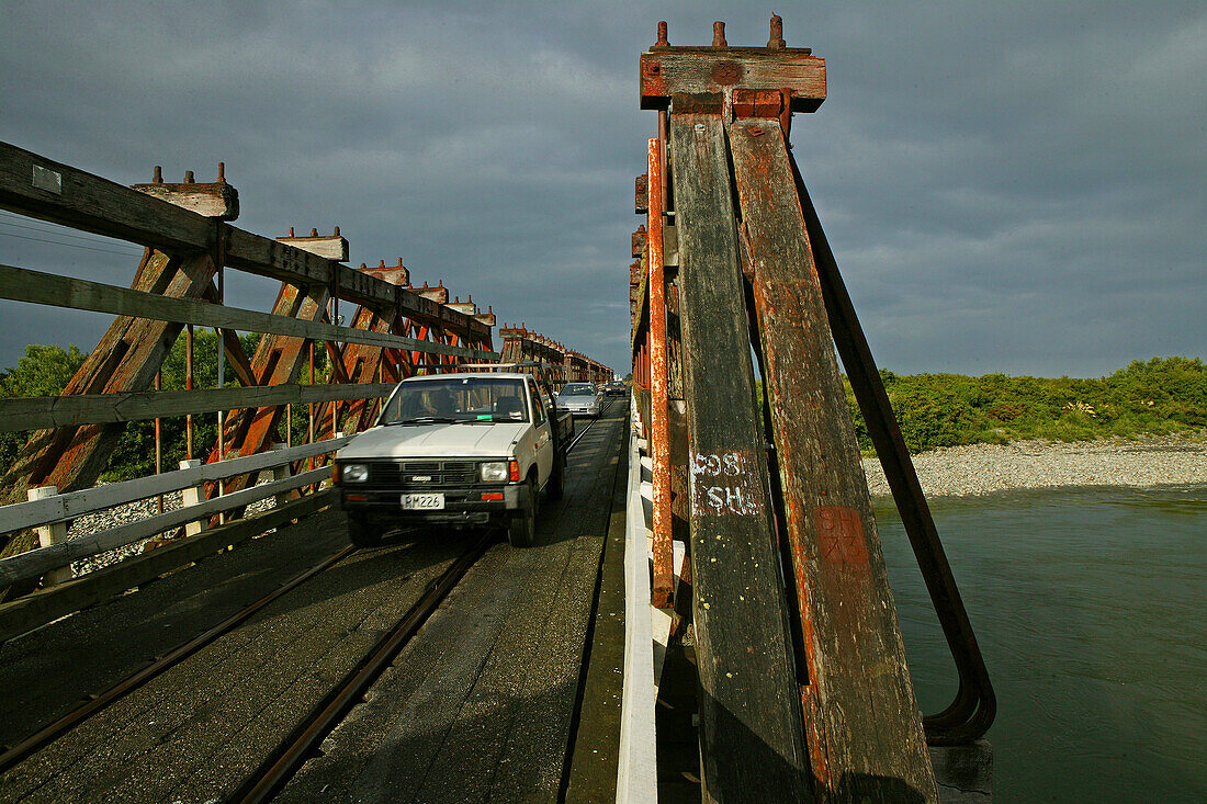 Holzbrücke unter Wolkenhimmel, Eisenbahn und Strassenverkehr teilen sich die schmale Brücke, Westküste, Südinsel, Neuseeland, Ozeanien