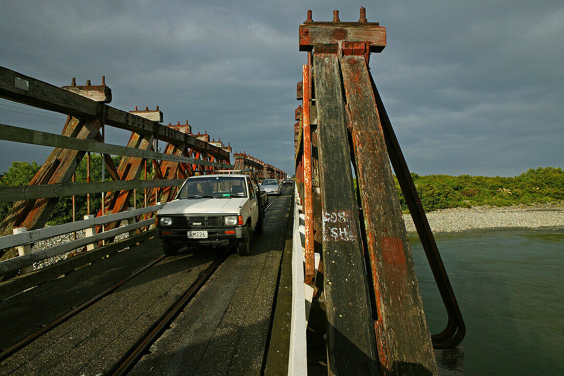 Wooden bridge under clouded sky, traffic and railway sharing the narrow bridge, West Coast, South Island, New Zealand, Oceania