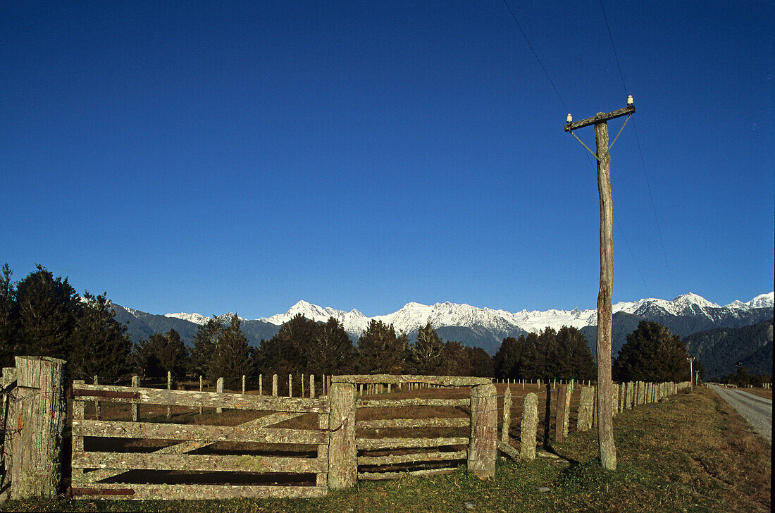 View of weathered fence in front of snow covered Southern Alps, West Coast, South Island, New Zealand, Oceania