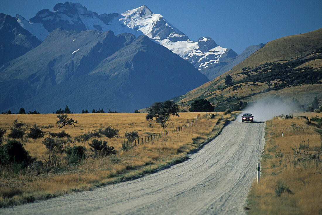 Country road with car in front of snowy mountains, Central Otago, South Island, New Zealand, Oceania