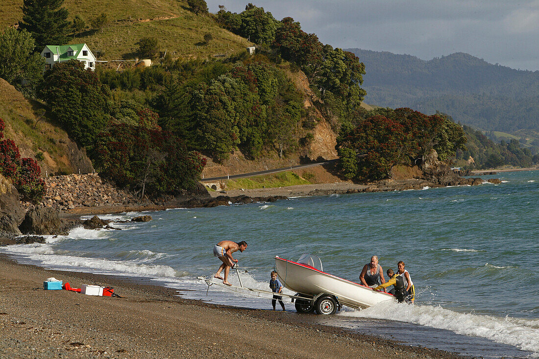Menschen am Strand lassen ein Boot zu Wasser, Oamaru Bucht, Coromandel Halbinsel, Pohutukawa Küste, Nordinsel, Neuseeland, Ozeanien