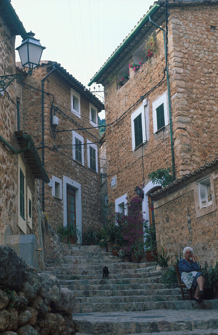 Alte Frau sitzt auf Steintreppen, Gasse in Fornalutx, Mallorca, Balearen, Spanien