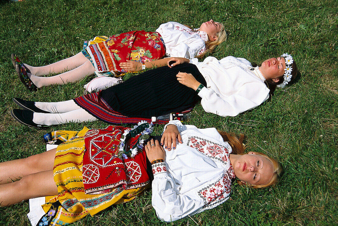 Young women in traditional costumes sunbathing on meadow, traditional celebration, Tallinn, Estonia
