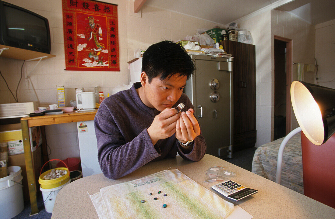 Chinese opal buyer, Chan, Lightning Ridge, Australien, NSW, Chinese opal buyer inspecting local stones. The town known as The Ridge is near the Queensland border.The opal is Australia's national stone and a popular souvenir. Chinesische Opalkäufer in Blac