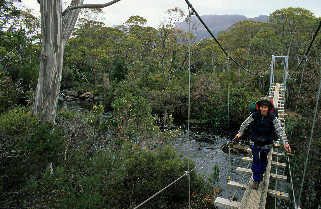 Bridge crossing, Cradle Mountain National Park, Australia, Tasmania, woman crossing Narcissus River on swing bridge, Overland Track