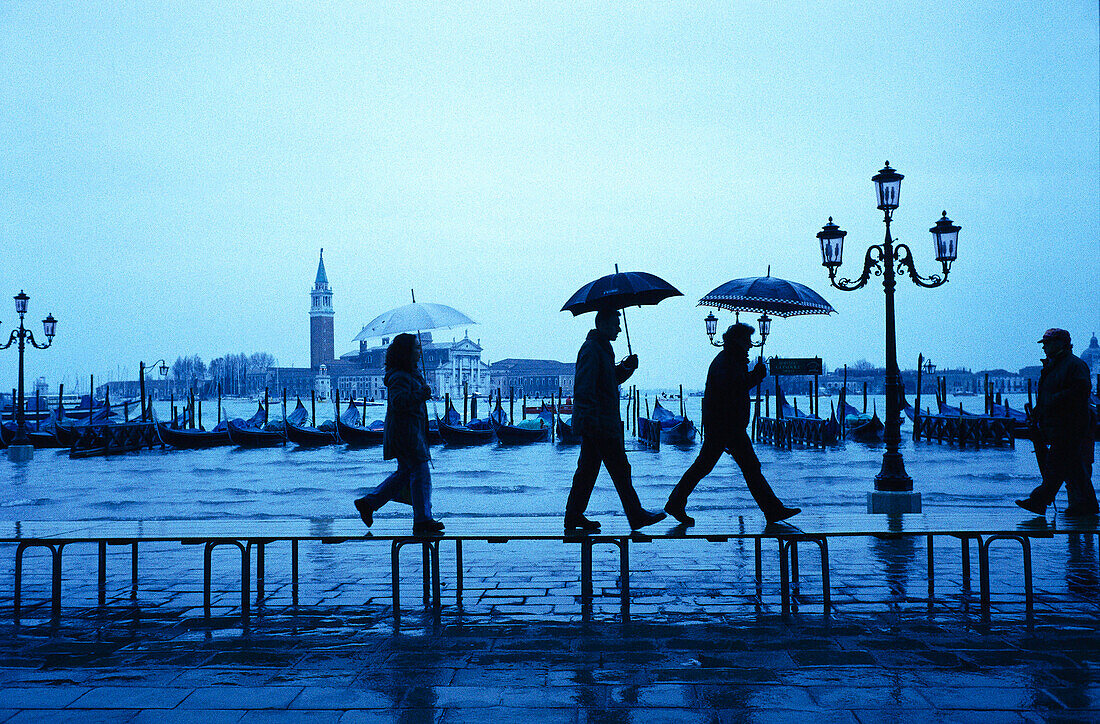 Passanten laufen im Regen über den überfluteten Georgio Maggiore in Venedig, Italien