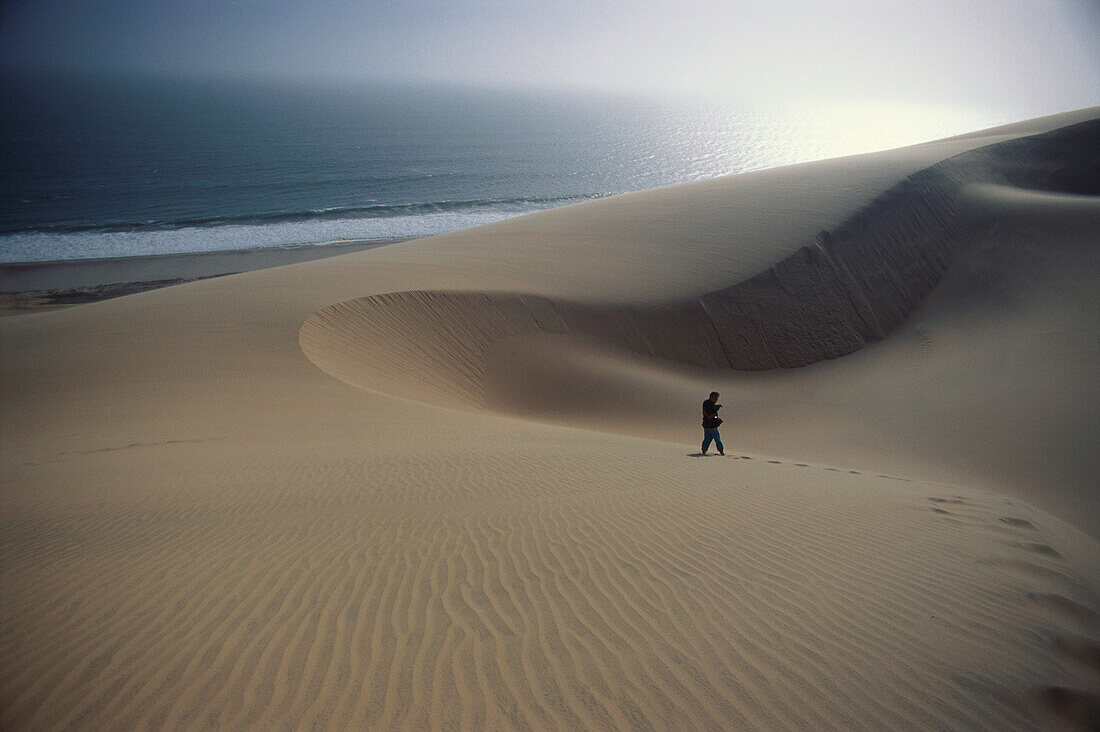 Eine Person geht über Dünen am Meer, Sandwich Harbour, Namib, Naukluft Park, Namibia, Afrika