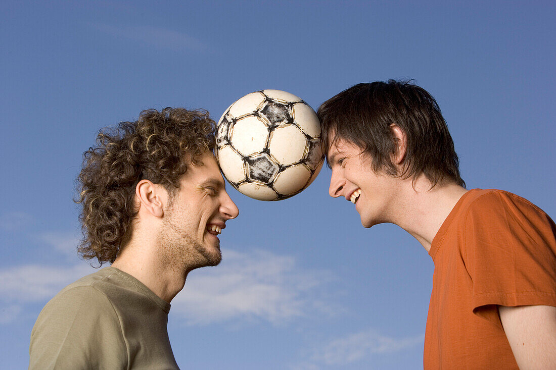 Zwei junge Männer halten Fußball zwischen ihren Köpfen