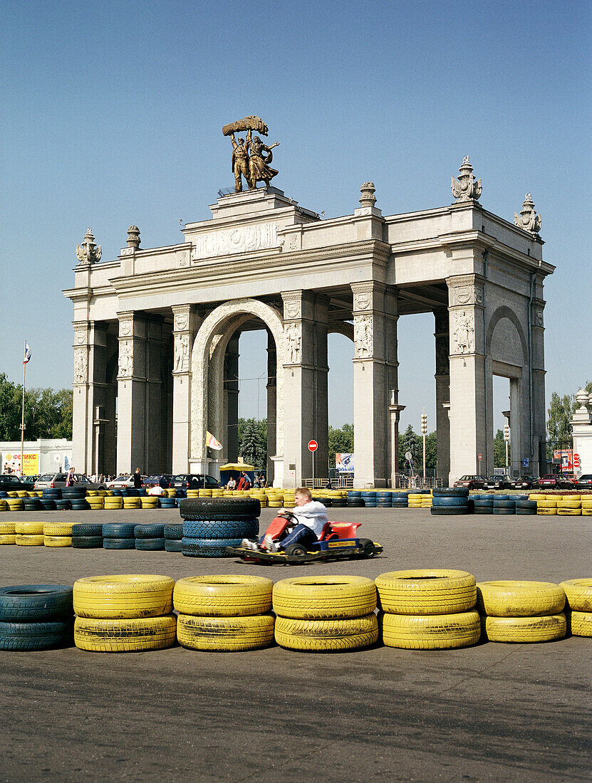 Man driving a go-kart in front of a main entrance to All-Russia Exhibition Centre, Moscow, Russia