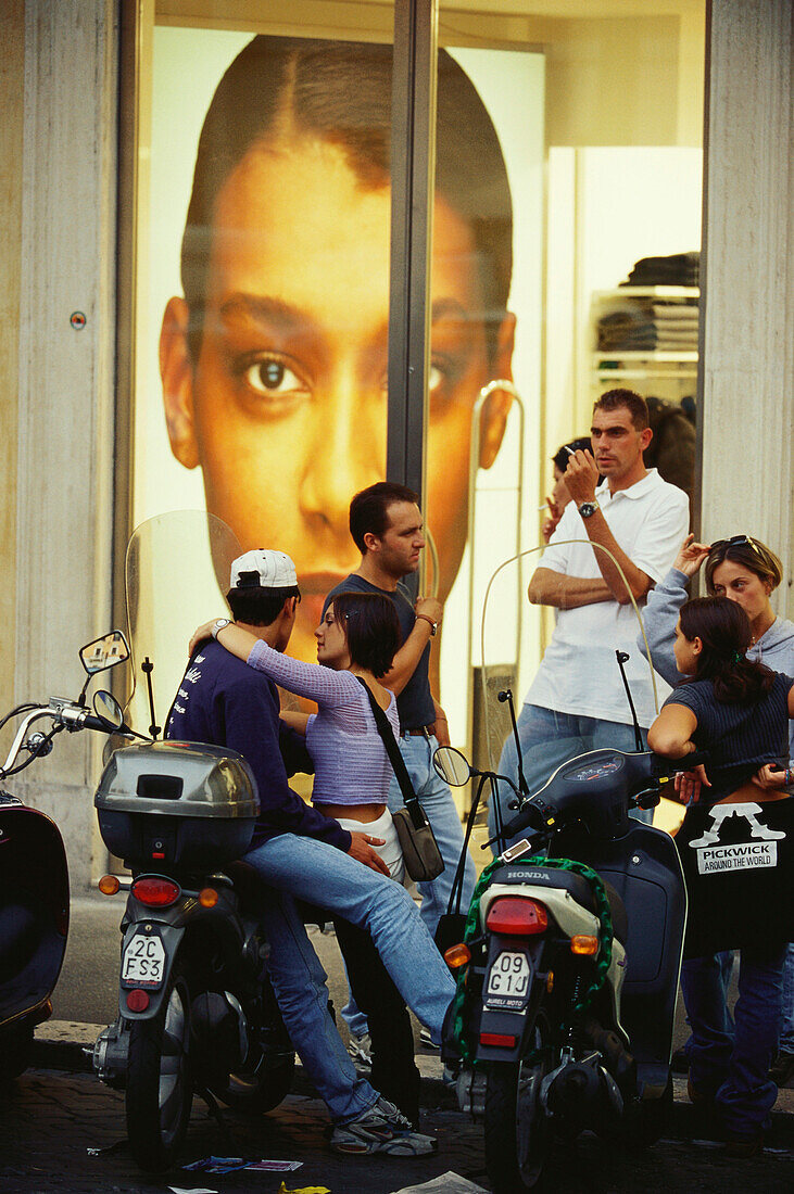Junge Leute mit Motorrollern vor einem Werbeplakat, Rom, Italien, Europa