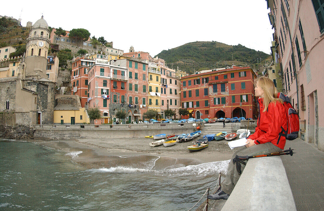 Eine Frau sitzt auf dem Hafenmauer, Entspannung nach einer Wanderung, Riomaggiore, Cinque Terre, Italy.