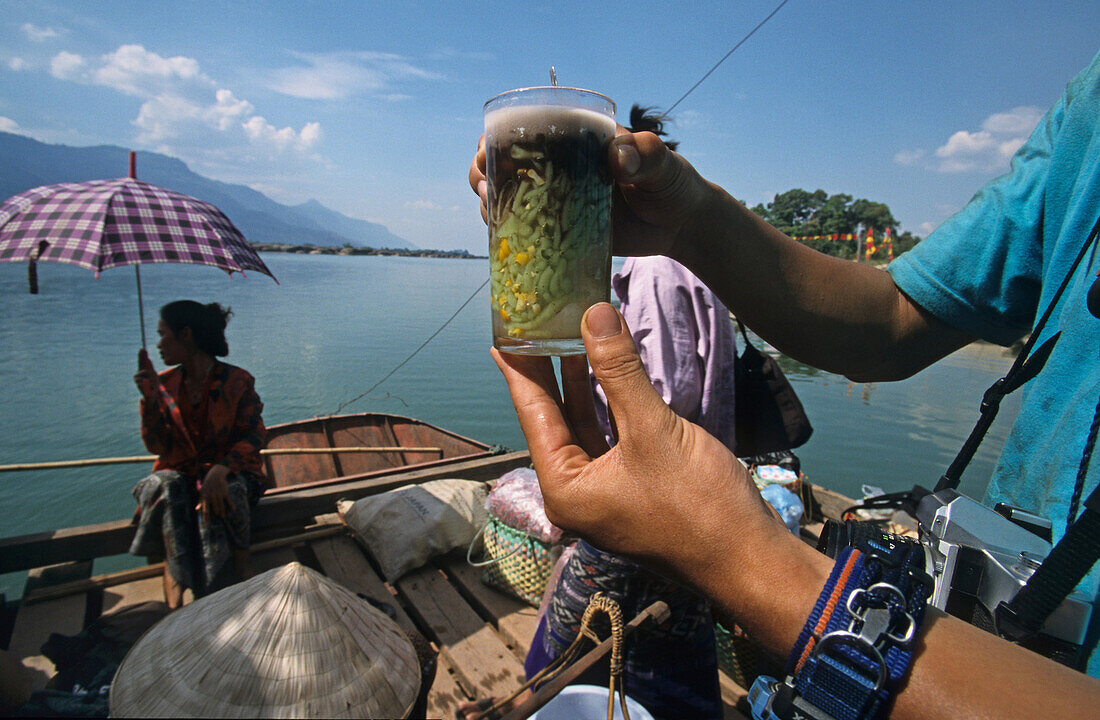 Person mit Fruchtgetränk auf einer Fähre, Laos