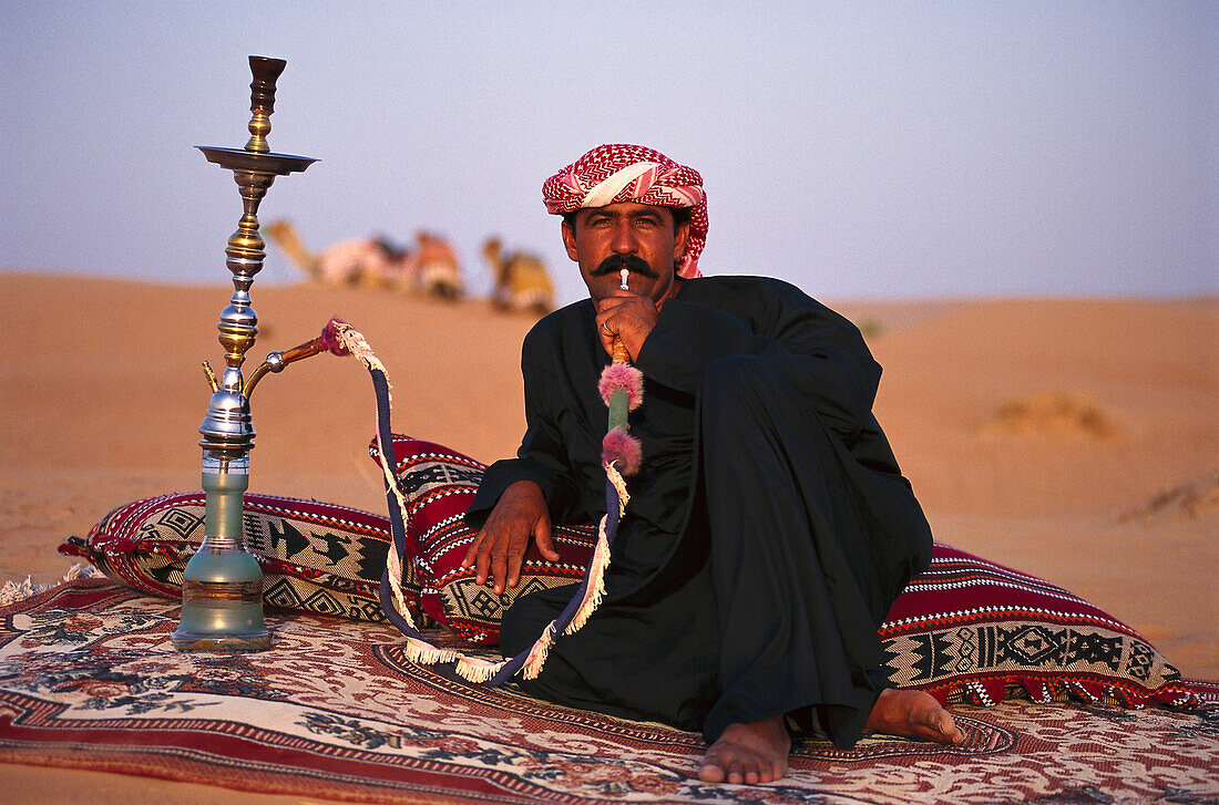 Beduine mit Wasserpfeife in der Wüste am Abend, Dubai, V.A.E., Vereinigte Arabische Emirate, Vorderasien, Asien