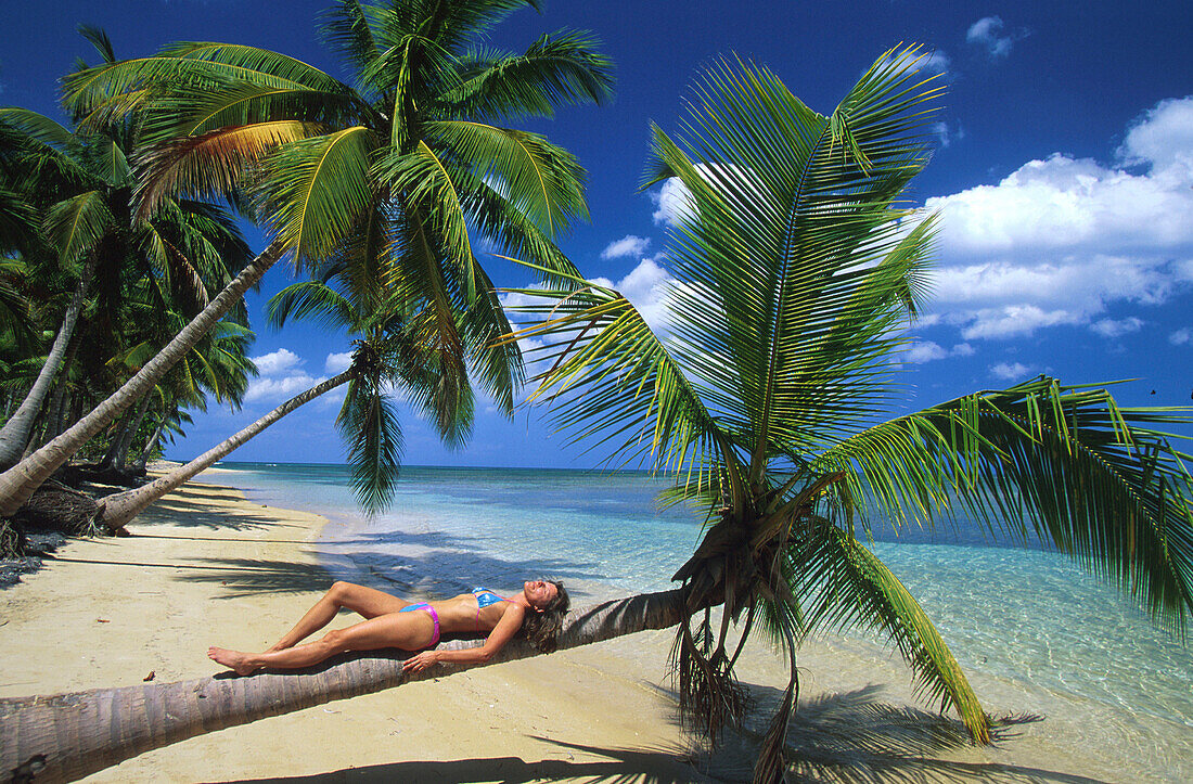 Woman lying on palm tree, sandy beach, Dominican Republic