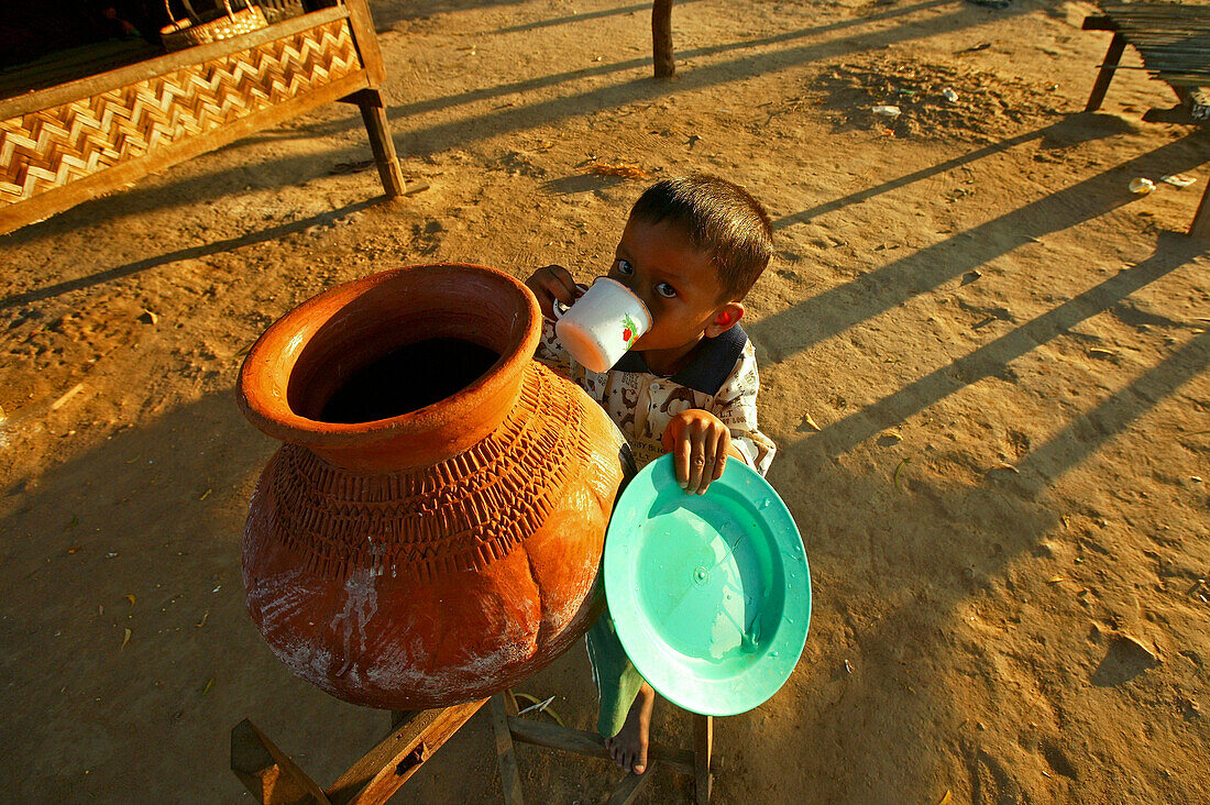 Child drinks water from terracotta pot, Kind trinkt Wasser aus dem Tontopf, Tonkrug, diese Wasserbehaelter stehen ueberall in Burma