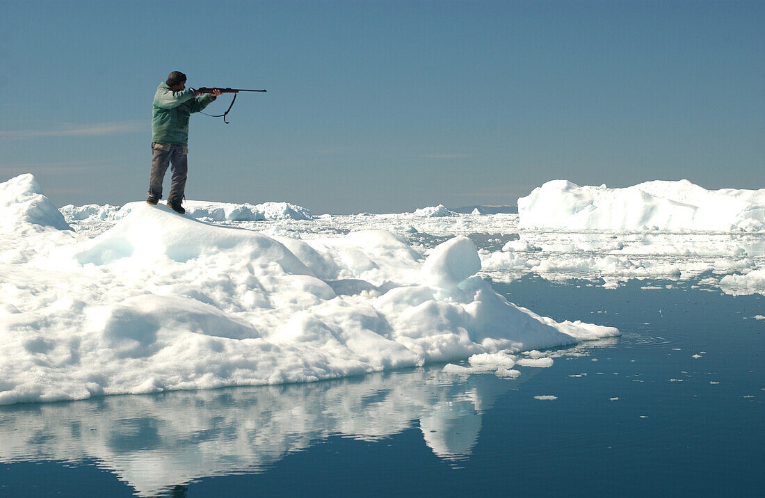 Jäger mit Gewehr steht am Wasser, Ilulissat, Grönland