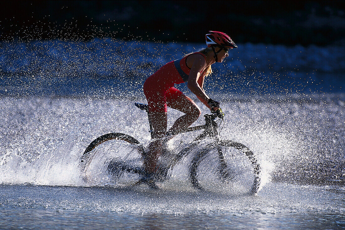 Female mountainbiker passing river, Bavaria, Germany