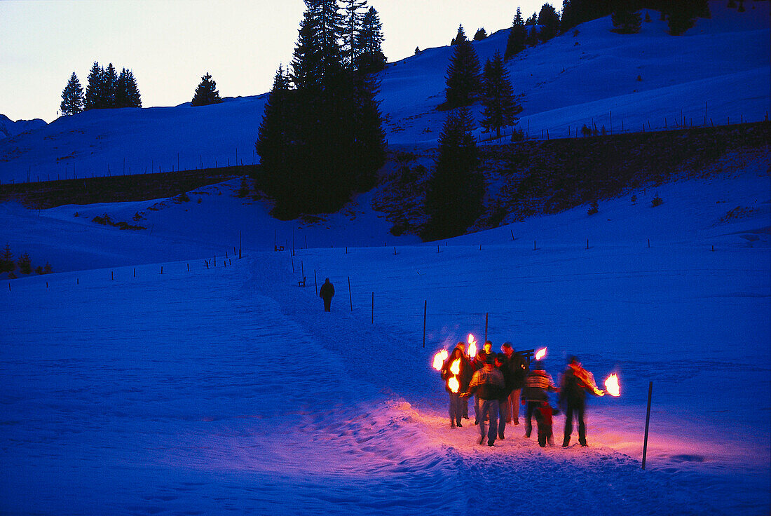 People walking with torches through snowcovered scenic, Arlberg, Vorarlberg, Austria