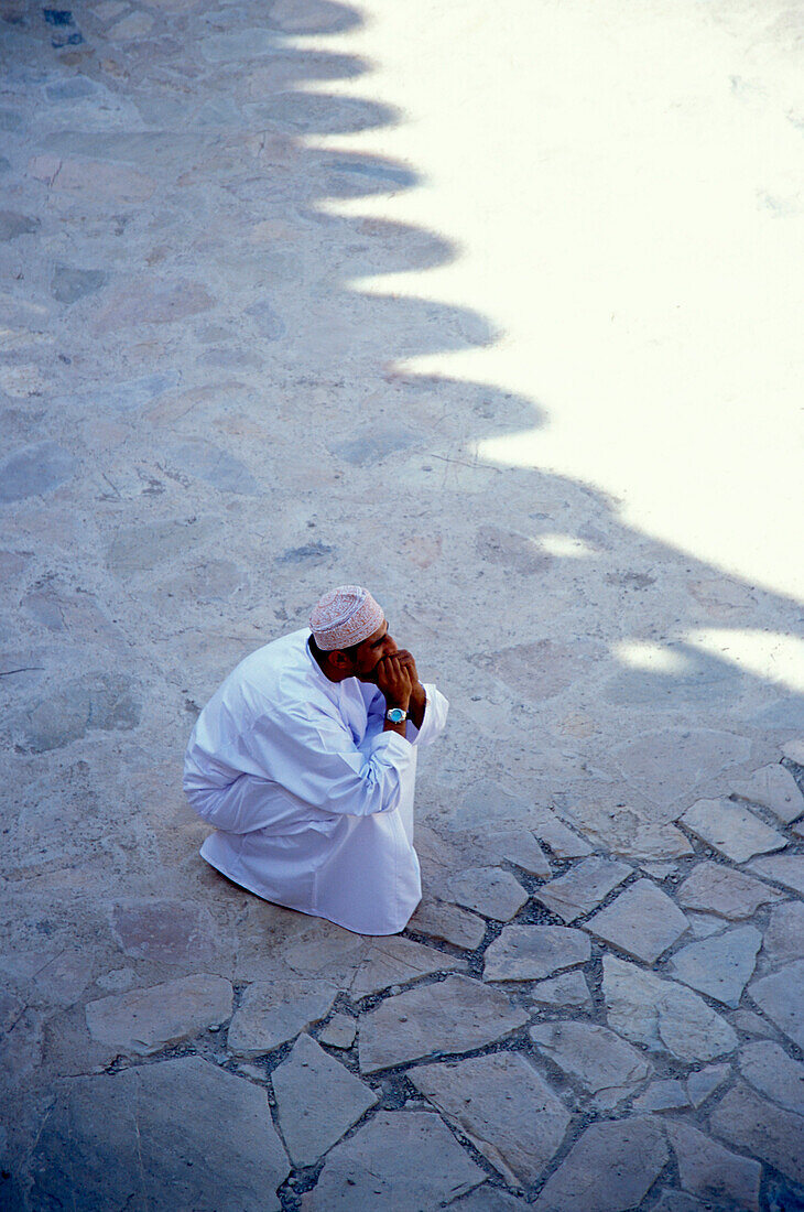 Ein Mann hockt im Schatten, Nizwa, Oman