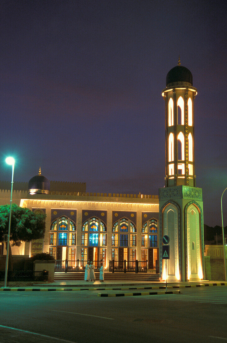 Menschen stehen nachts vor einer beleuchteten Moschee, Maskat, Oman