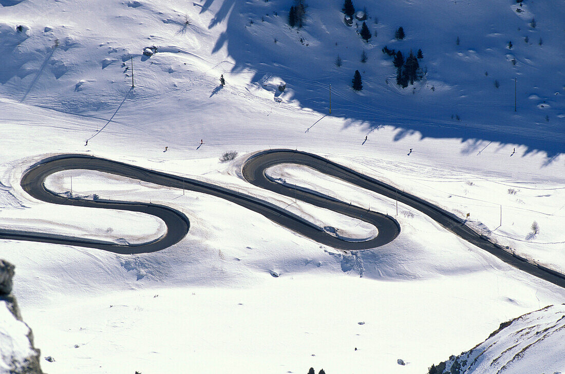 Menschen fahren Ski auf einer Piste neben einer Serpentine, Passo Pordoi, Südtirol, Italien