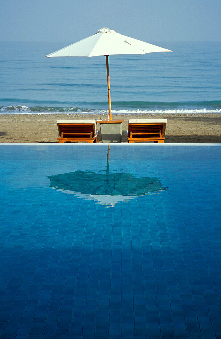 Ein Sonnenschirm spiegelt sich im Pool des Chedi Hotel, Maskat, Oman