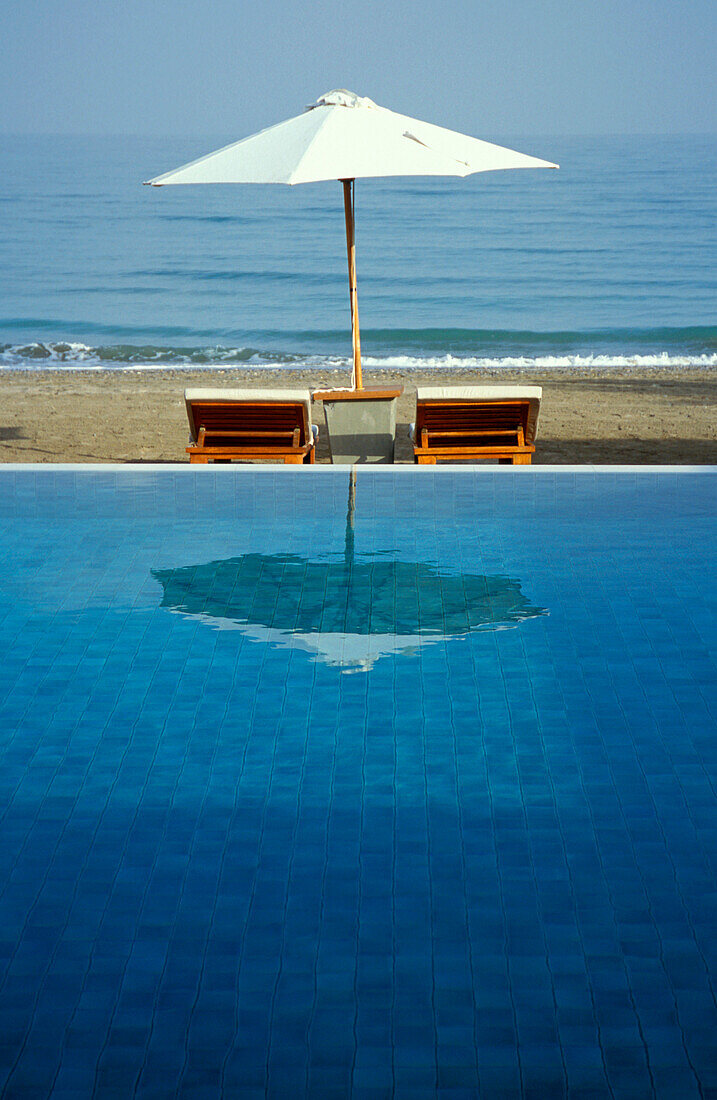 The pool of the Chedi Hotel reflecting a sunshade, Muscat, Oman