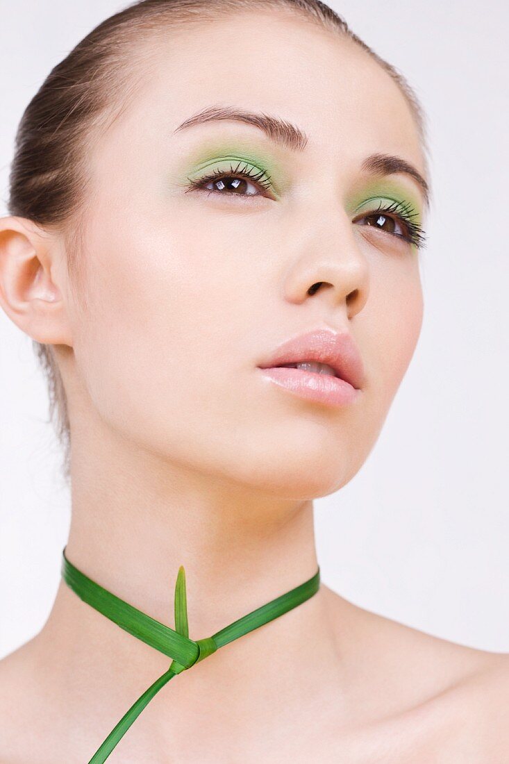 A young woman with green make-up with a plant around her neck