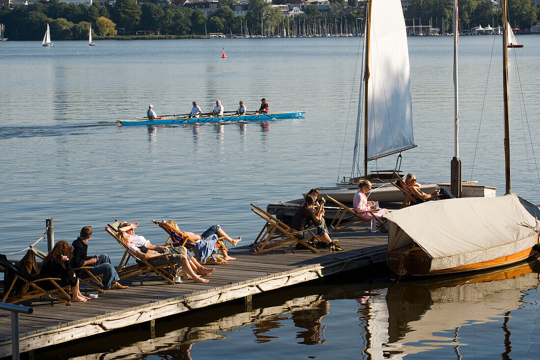 People sitting on deck chairs at lake Alster, rowingboat in background, Hamburg, Germany