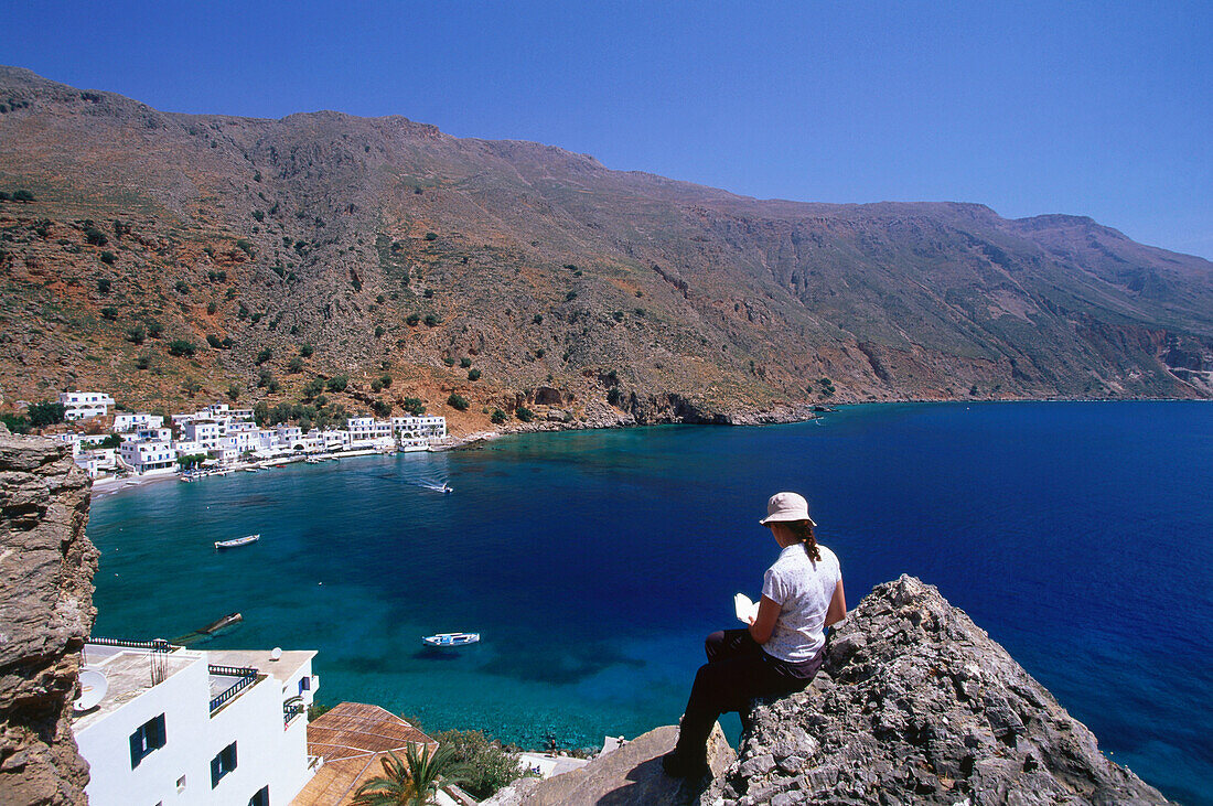 Woman sitting on rock above bay, Loutro, Crete, Greece
