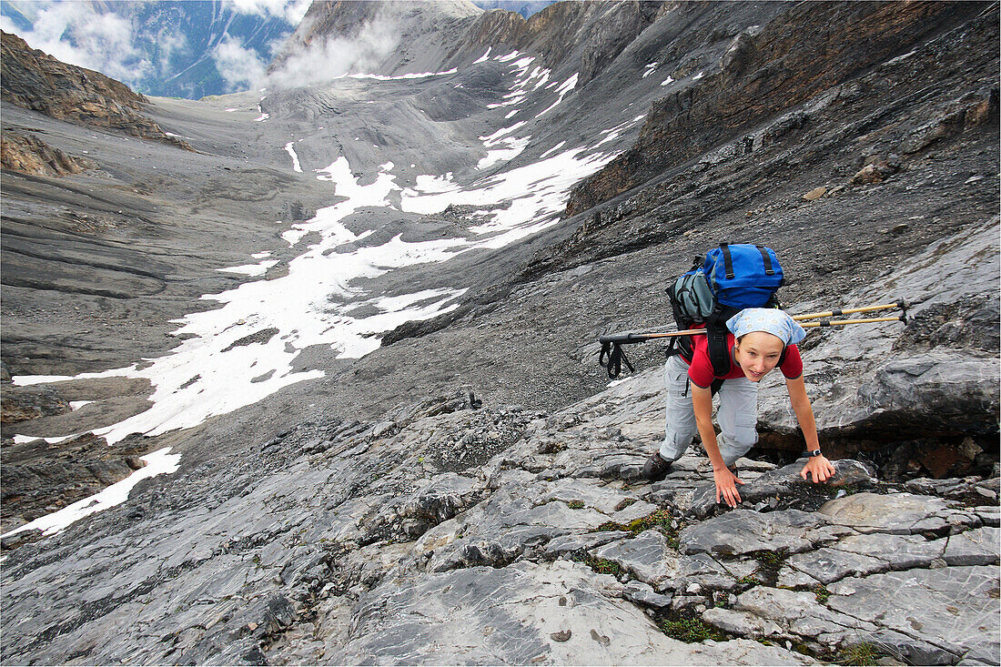 Frau klettert über eine Felsstufe auf einer abenteuerlichen Wanderung, Piz Quattervals, Valetta, Schweizer Nationalpark, Engadin, Graubuenden, Graubünden, Schweiz, Alpen