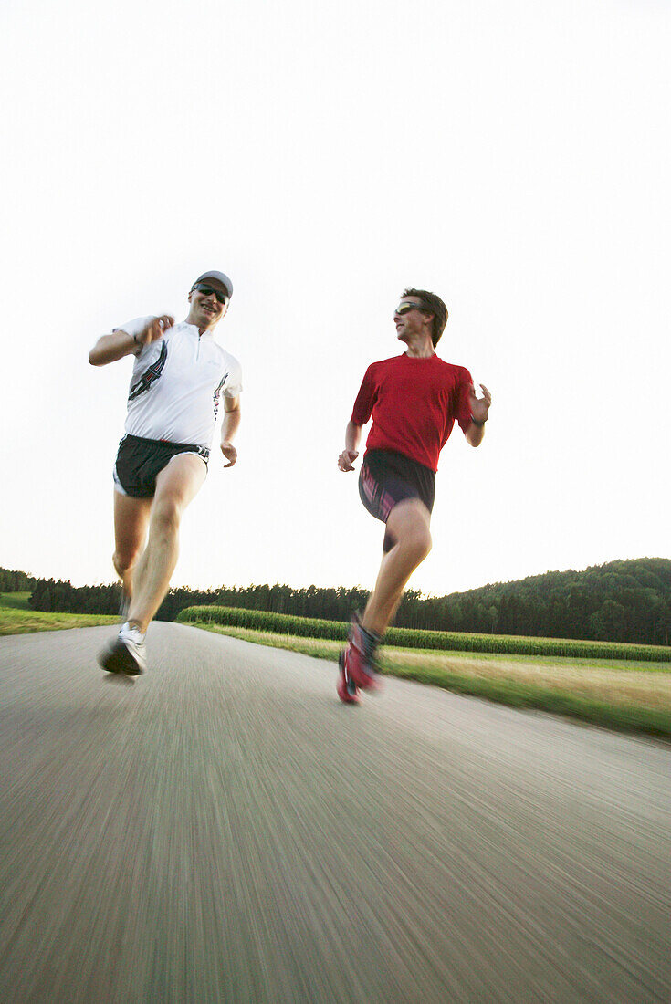 Zwei junge Männer joggen auf Landstrasse