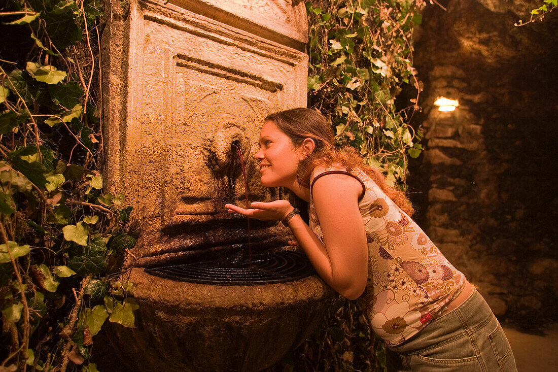 Woman at wine fountain in Buda Castle Labyrinth, Woman tasting red wine of the wine fountain in Buda Castle Labyrinth, Buda, Budapest, Hungary