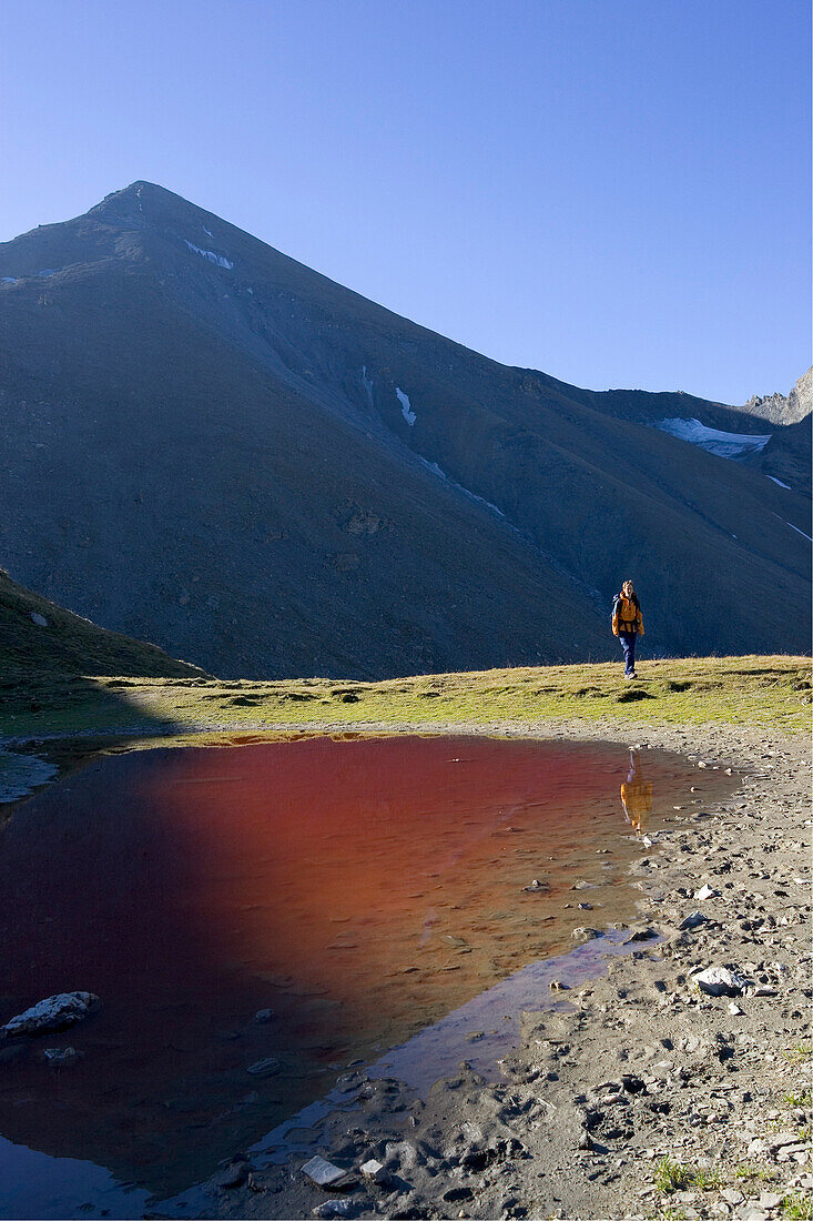 Junge Frau wandert am Roten Seeli vorbei, gefaerbt von roten Algen. Samnaun, Unterengadin, Graubünden, Schweiz