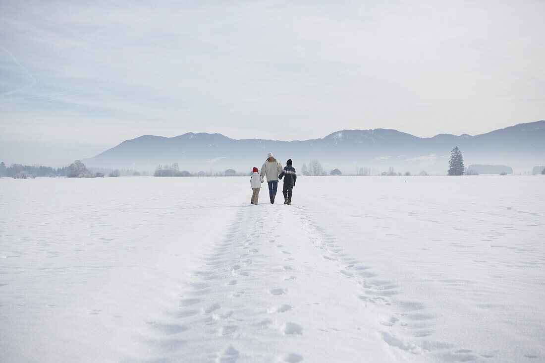 Mutter mit zwei Kindern Hand in Hand im Schnee