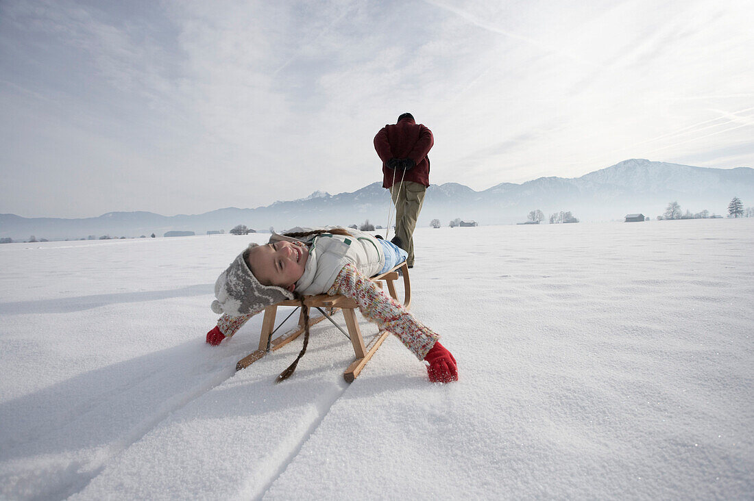 Man pulling daughter in toboggan on snow